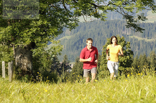Young couple jogging in meadow  mountains in background