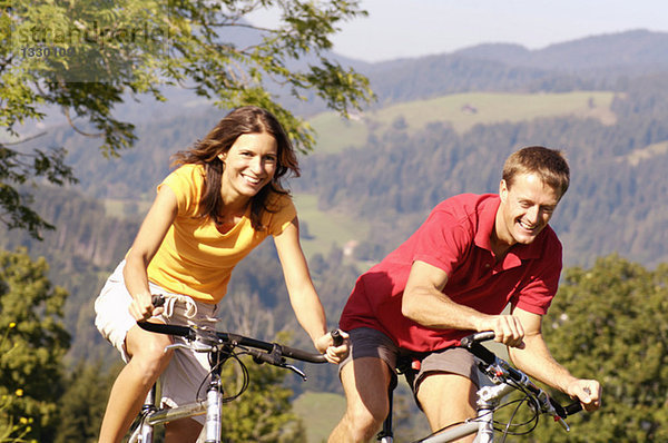 Junges Paar beim Radfahren  lächelnd  Berge im Hintergrund