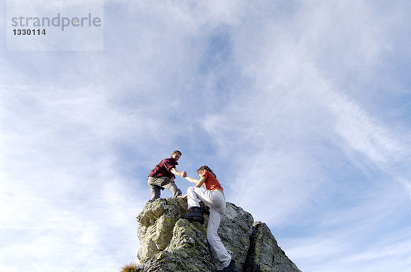 Junges Paar  das auf den Berggipfel klettert  Mann  der der Frau hilft  Blick in den niedrigen Winkel