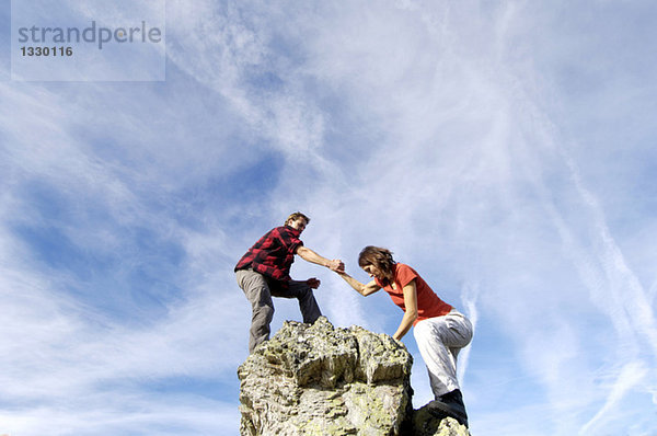 Junges Paar  das auf den Berggipfel klettert  Mann  der der Frau hilft  Blick in den niedrigen Winkel