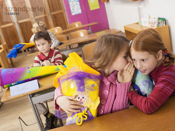 Mädchen (4-7) mit Schulkegel flüstern im Klassenzimmer  Neigungsansicht
