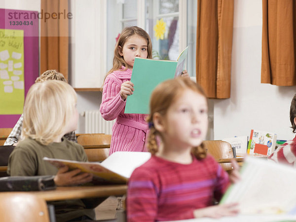 Kinder (4-7 Jahre) im Klassenzimmer  Schwerpunkt Mädchen-Lesebuch im Hintergrund