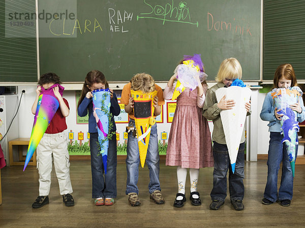 Kinder (4-7) stehen vor der Tafel und schauen in die Schultüte.