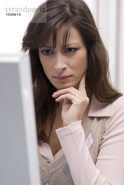 Junge Frau schaut auf Desktop-PC  Hand am Kinn  Nahaufnahme