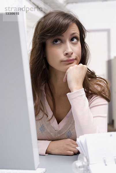 Junge Frau sitzt am Computer im Büro  schaut nach oben  Nahaufnahme