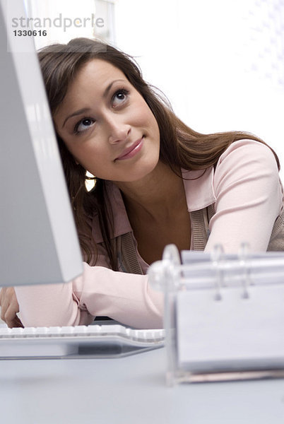 Junge Frau sitzt am Computer im Büro  schaut nach oben  lächelt