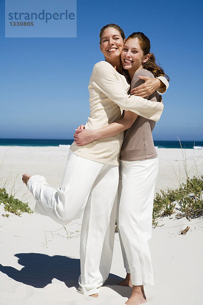 Mutter und Tochter umarmen sich am Strand