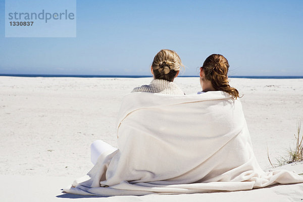 Mutter und Tochter sitzen am Strand  Rückansicht