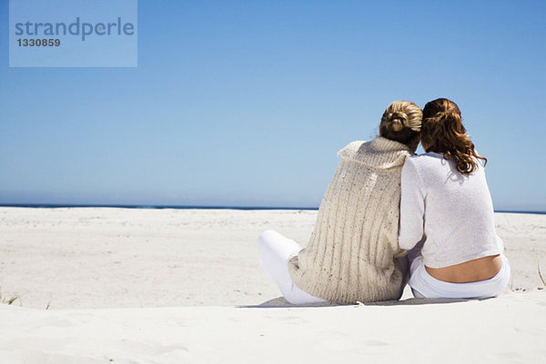 Mutter und Tochter sitzen am Strand  Rückansicht