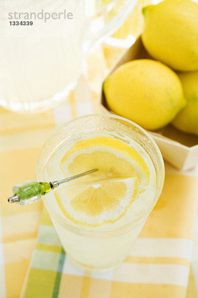 Zitronenlimonade im Glas mit aufgespiesster Zitronenspalte