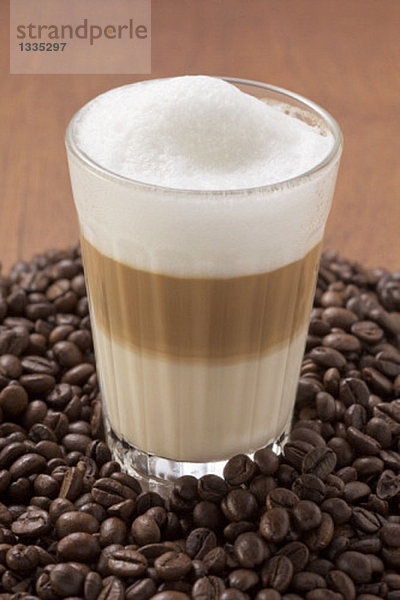 Ein Glas Latte Macchiato auf einem Haufen von Kaffeebohnen