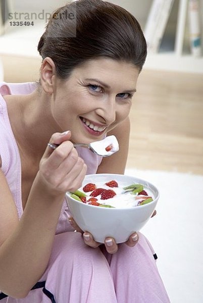 Frau isst Joghurt mit Kiwi und Erdbeeren