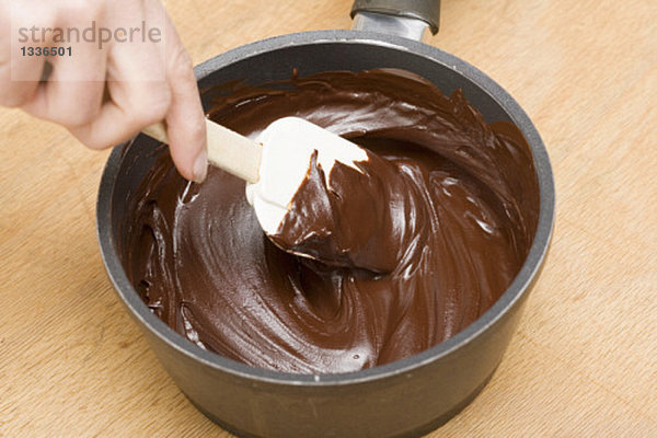 Geschmolzene Schokolade mit Teigschaber im Kochtopf verrühren