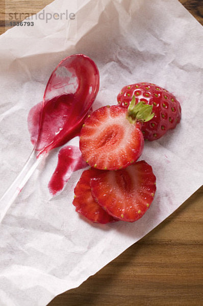 Ein Löffel Erdbeermarmelade und frische Erdbeeren auf Papier