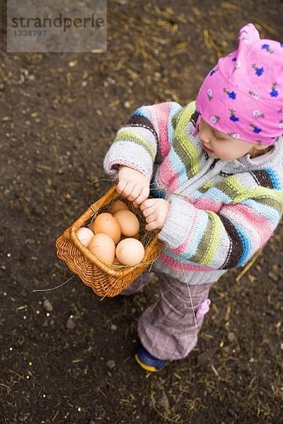 Kleines Mädchen hält Korb mit braunen Eiern