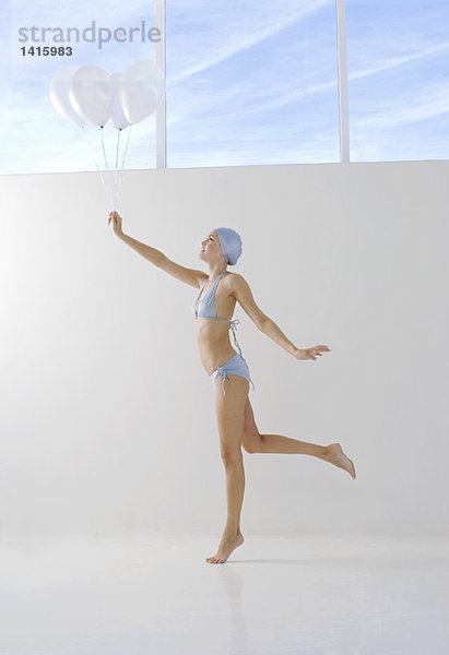 Junge Frau im Bikini und Badekappe mit weißen Luftballons