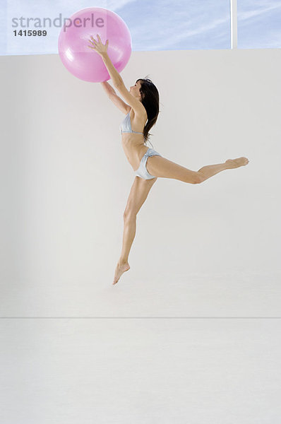 Junge Frau im Bikini  springend  mit großem rosa Luftballon