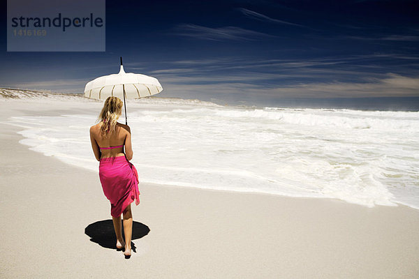 Junge Frau im Bikini und Pareo mit Sonnenschirm am Strand  Rückansicht