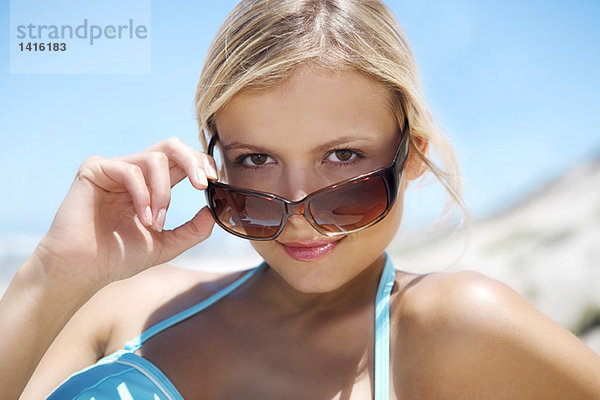 Porträt einer jungen Frau  die über ihre Sonnenbrille schaut