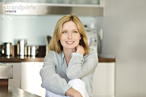 Lächelnde Frau in der Küche sitzend