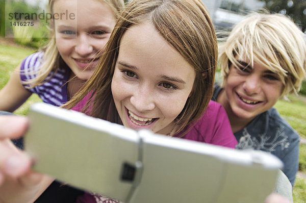 2 lächelnde Teenagermädchen und Junge mit Fotohandy im Freien