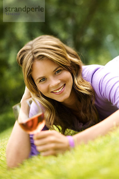 Junge lächelnde Frau auf Gras liegend  Glas Wein