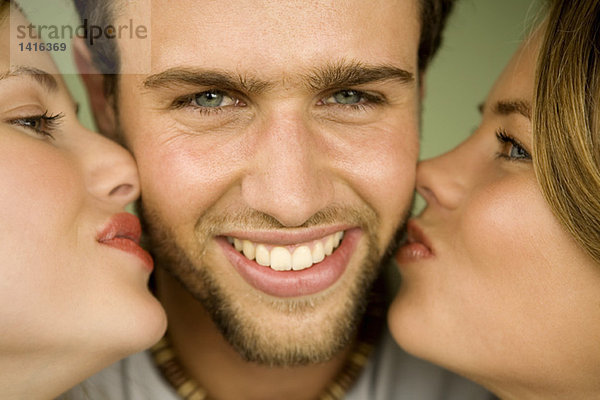 2 junge Frauen küssen lächelnden Mann