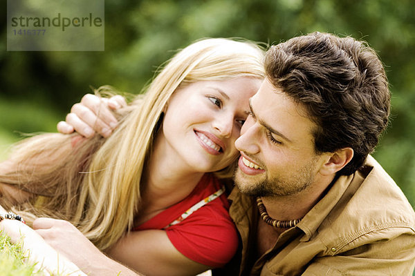 Porträt eines jungen lächelnden Paares  das sich im Freien umarmt.