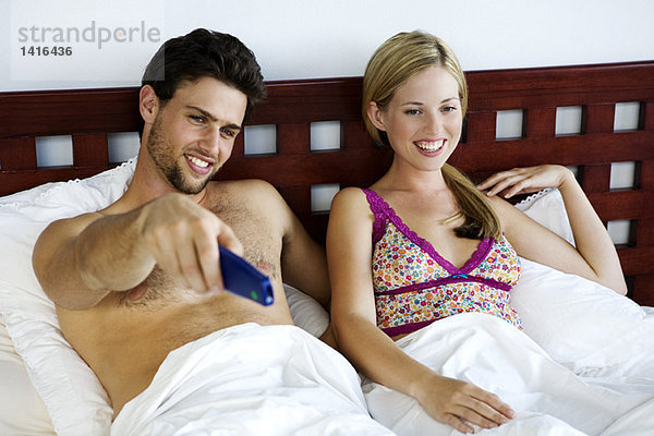 Junges lächelndes Paar im Bett  fernsehend