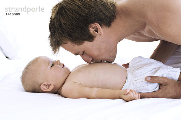 Porträt eines Vaters  der die Brust seines Babys küsst  auf dem Bett liegend  in Innenräumen.