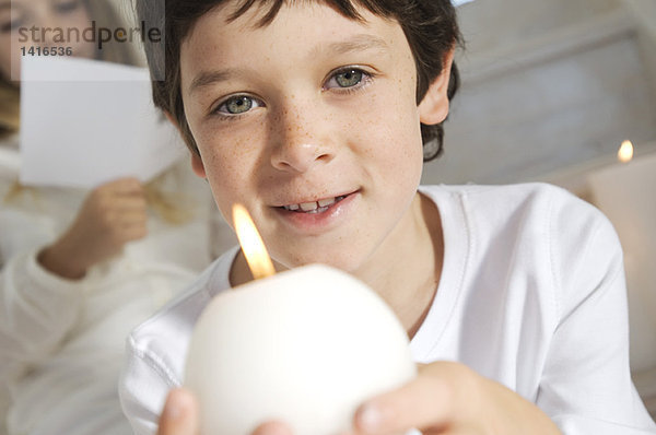 Porträt eines kleinen Jungen mit Kerze  Schwester im Hintergrund  drinnen