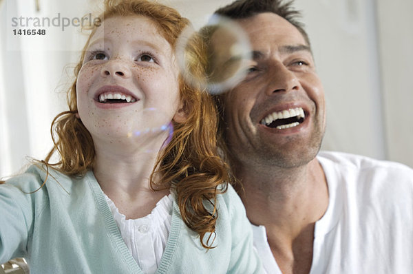 Porträt von Vater und Tochter beim Lachen  Blick auf Seifenblasen  drinnen