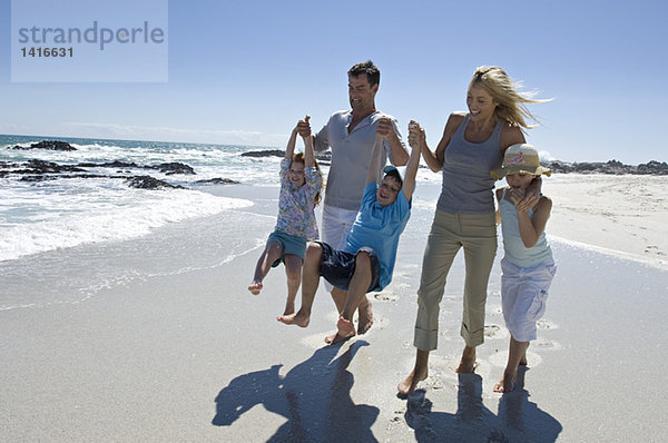 Eltern und drei Kinder beim Spaziergang am Strand  im Freien