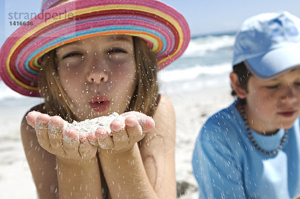 Porträt eines kleinen Mädchens  das Sand in die Hände bläst  Junge im Hintergrund  draußen