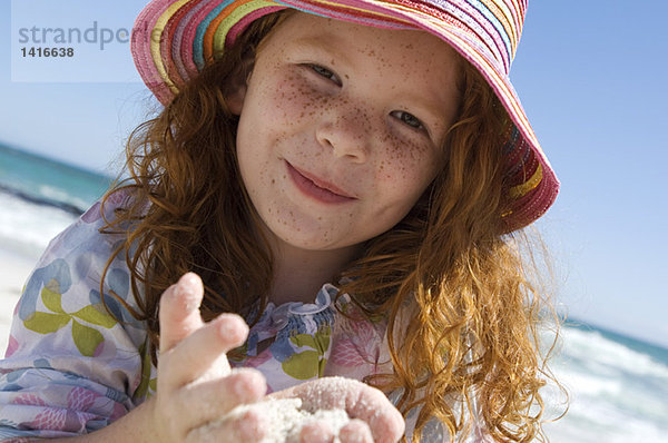 Porträt eines kleinen Mädchens  das lächelnd in die Kamera schaut  Sand in den Händen  im Freien