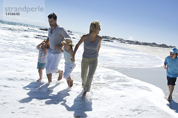 Eltern und drei Kinder beim Spaziergang am Strand  im Freien