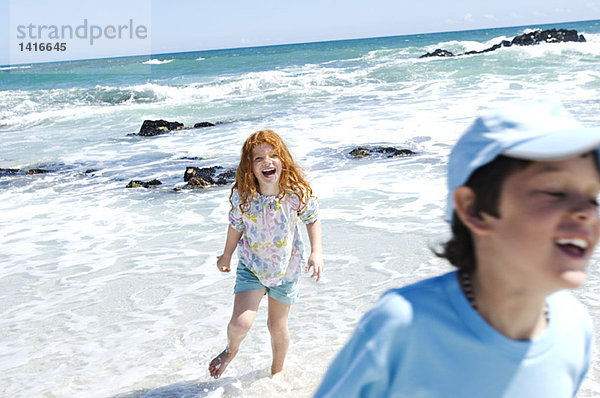 Junge und kleines Mädchen gehen am Strand spazieren  im Freien