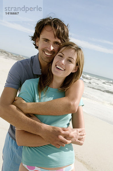 Paar in einer Umarmung  am Strand  für die Kamera posierend  im Freien