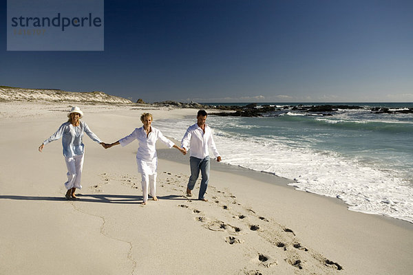 Ehepaar und Seniorin halten sich am Strand an den Händen.