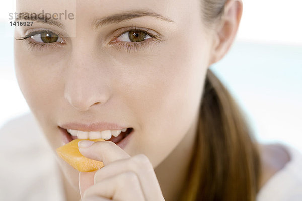 Porträt einer jungen Frau  die ein Stück Melone isst  drinnen