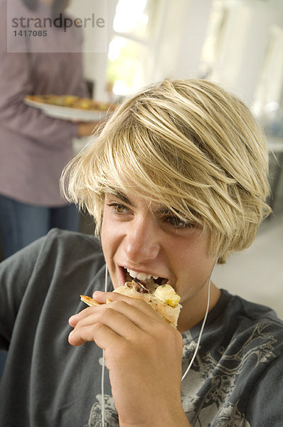 Porträt eines Teenagers beim Essen  Frau im Hintergrund