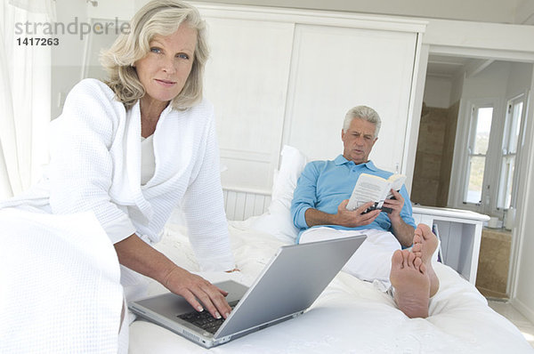 Paar im Bett  Mann lesend  Frau mit Laptop