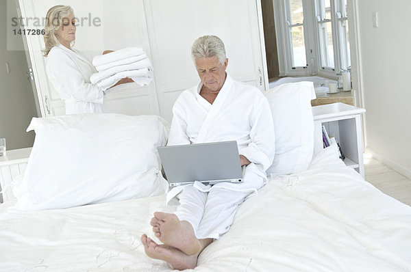 Paar im Schlafzimmer  Frau mit Handtuchstapel  Mann mit Laptop