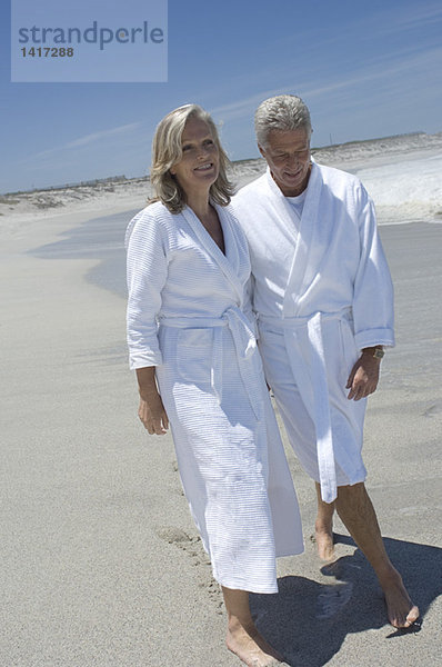 Paar im Bademantel am Strand spazieren gehen