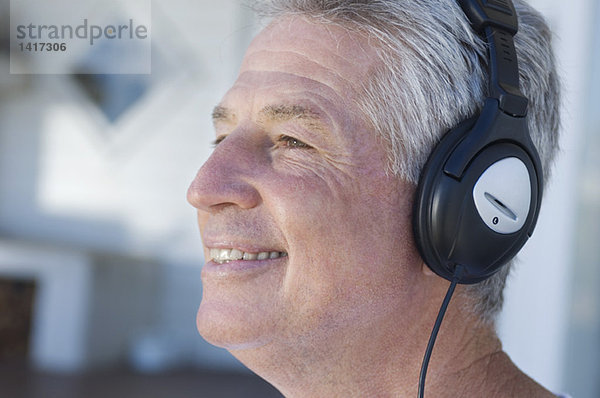 Porträt eines lächelnden Mannes  der mit Kopfhörern Musik hört.