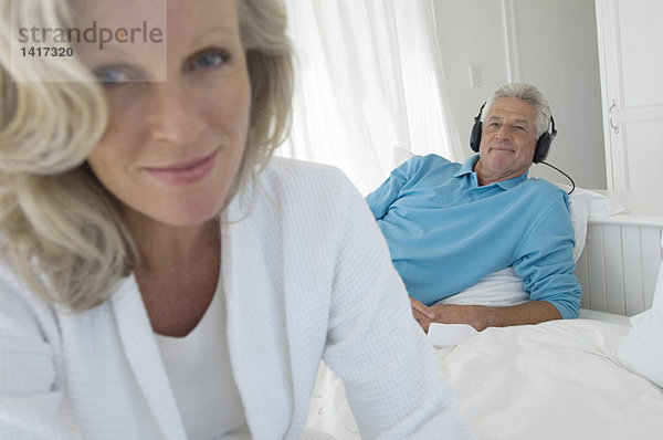 Paar im Schlafzimmer  Frau schaut in die Kamera  Mann hört Musik mit Kopfhörer im Hintergrund