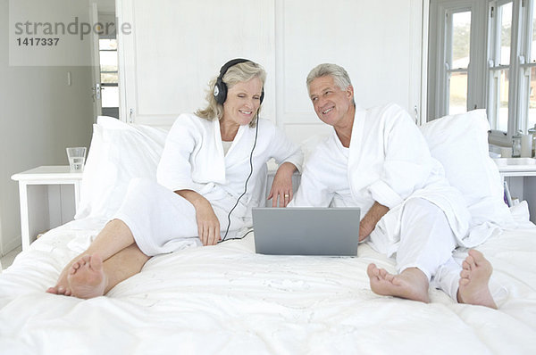 Paar im Bademantel mit Laptop im Bett