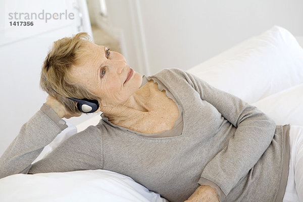 Seniorin auf dem Bett liegend  Musik hören mit Kopfhörer