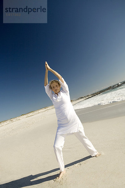 Seniorin beim Yoga am Strand