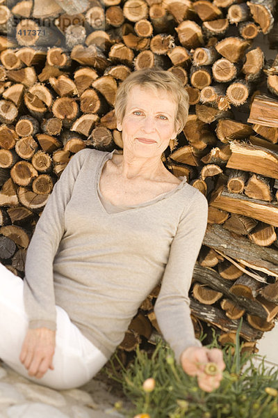 Seniorin sitzend am Holzhaufen